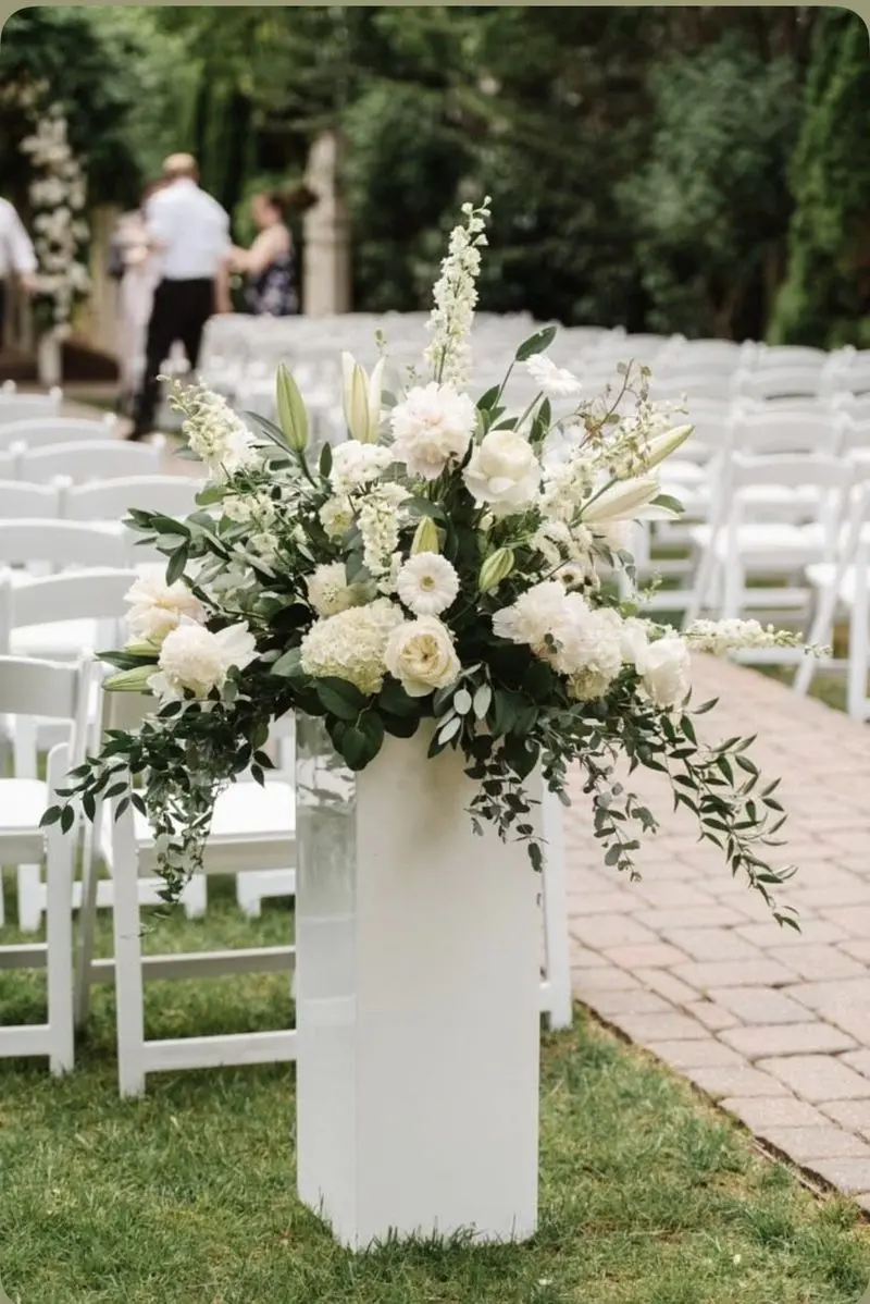 Garden-style white floral pedestal arrangement along a brick ceremony aisle