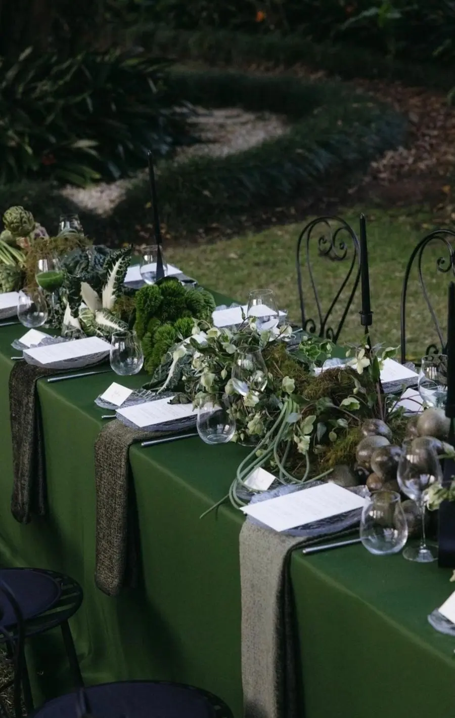 Garden table with a forest green tablecloth and a mossy foliage centerpiece with black taper candles