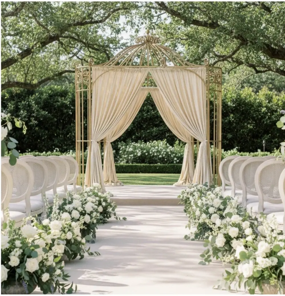 Gold ceremony arbor draped in fabric, flanked by white floral aisle arrangements