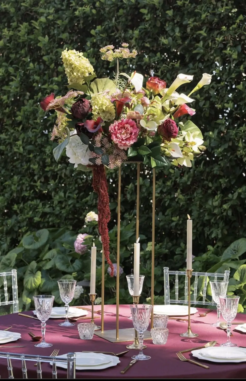 Jewel-toned floral arrangement in burgundy, blush, and cream on a garden party table