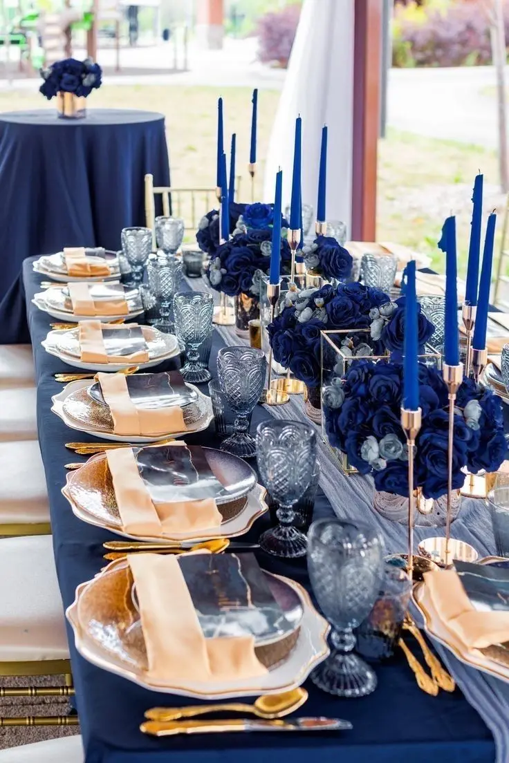 Long navy table with navy rose centerpieces, navy taper candles and gold flatware