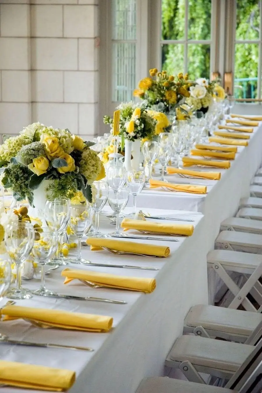 Long white table with yellow napkins and yellow and green floral centerpieces