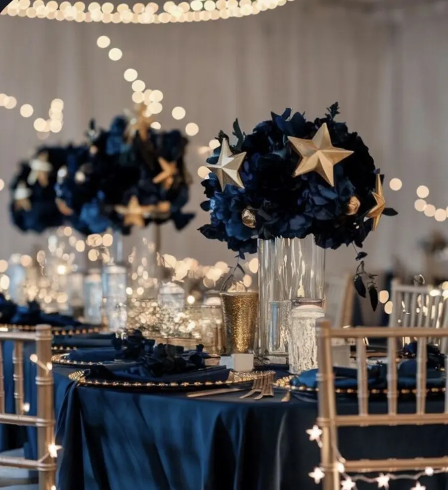 Navy hydrangea centerpieces with gold stars on a navy-draped table under string lights