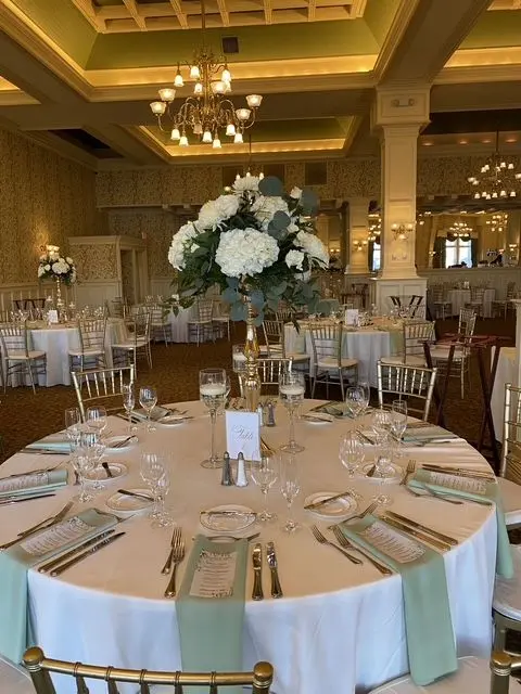 Round banquet table with a tall white hydrangea centerpiece and sage green napkins in a ballroom