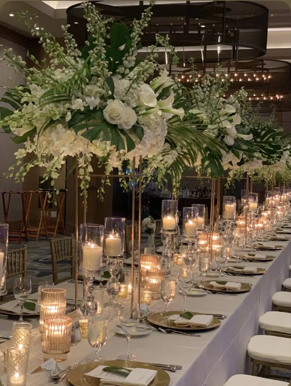 Tall white floral centerpieces along a reception table with gold accents
