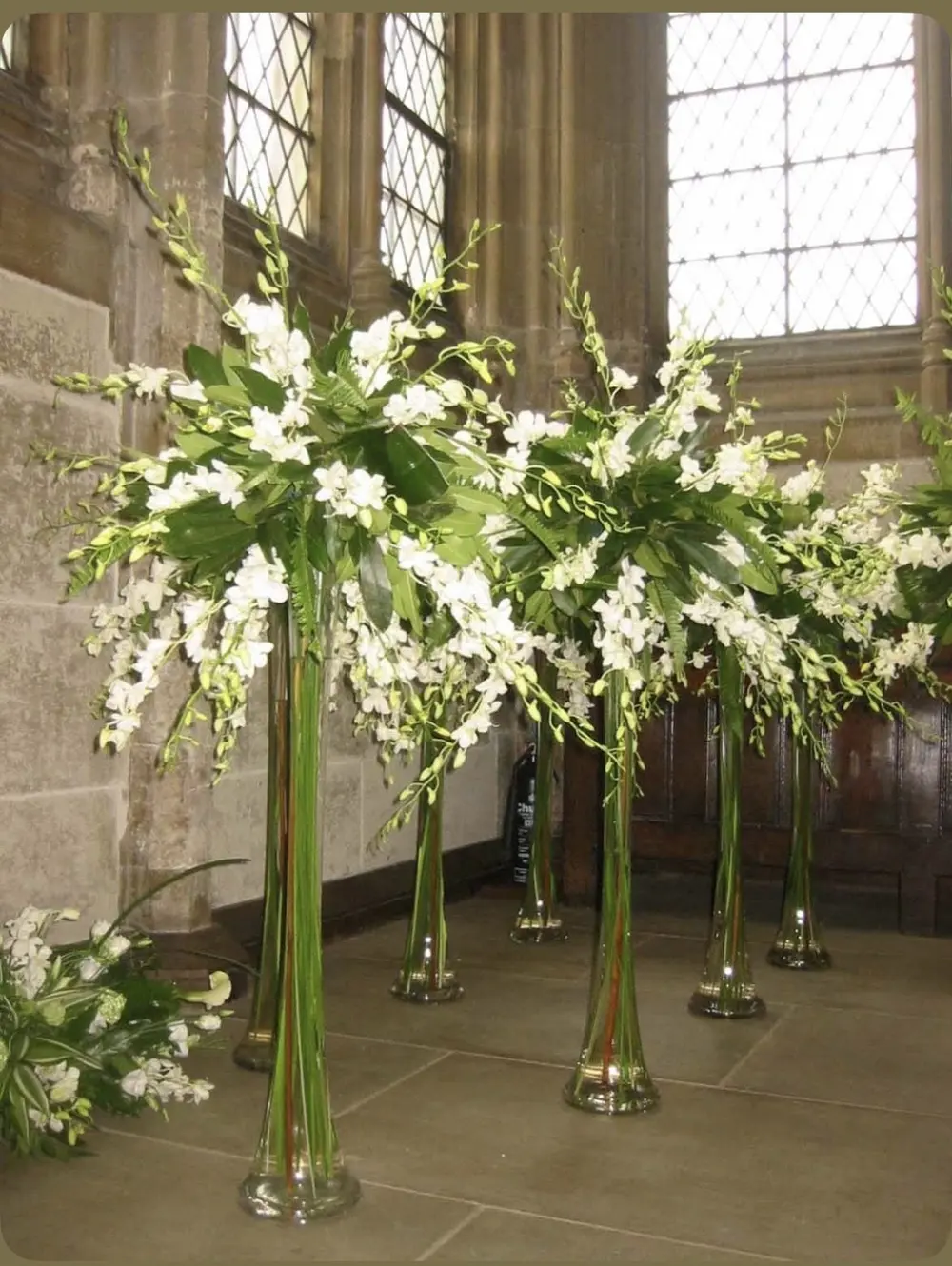 Tall white orchid arrangements lining a stone church aisle