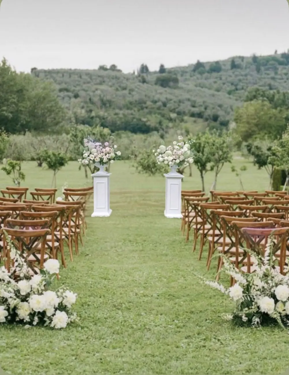 White and blush floral pedestal arrangements framing an outdoor ceremony aisle