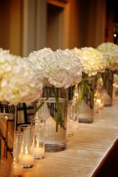 White hydrangea blooms in glass vases lined along a candlelit table